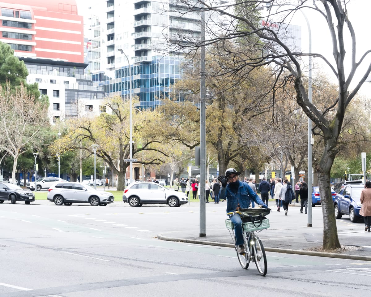 Tin, on his bicycle, is crossing the street giving the photographer a wave